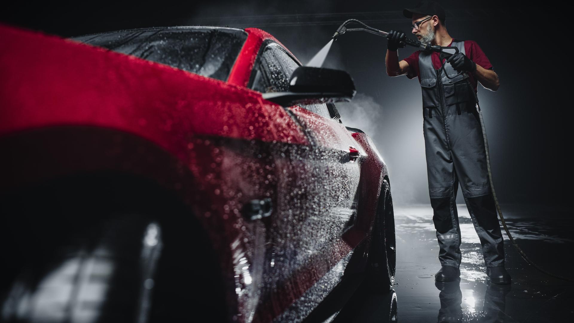 Advertising Style Photo of a Professional Car Wash Specialist Using a High Pressure Washer to Clean and Prepare a Red Sports Coupe for Detailing, Polishing and Waxing